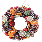 A festive winter wreath decorated with pinecones, dried orange slices, red berries, green melons, and star anise on a white background.
